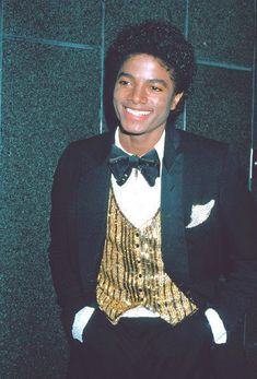 a young man in a tuxedo smiles for the camera while standing next to a wall