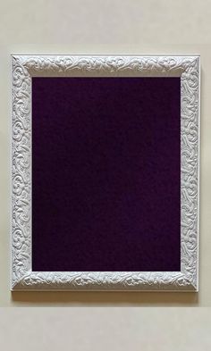 an empty white frame hanging on the wall with purple paper in it's corner