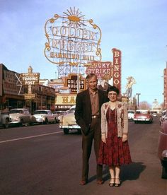 a man and woman standing in front of a neon sign on the las vegas strip