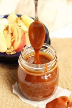 caramel sauce being poured into a jar with apples in the background on a table