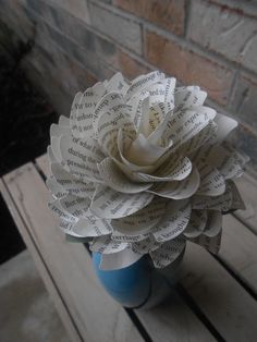 a blue vase filled with paper flowers on top of a wooden table next to a brick wall