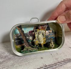 a miniature tin with an elephant and dog in it on a table next to a hand