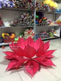 a large red paper flower sitting on top of a white tile floor next to shelves