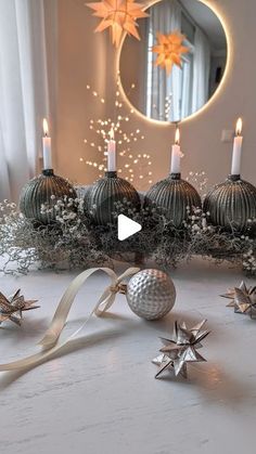 a white table topped with silver balls and stars next to a candle holder filled with christmas decorations