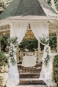 an outdoor gazebo decorated with white flowers and greenery for a wedding or reception