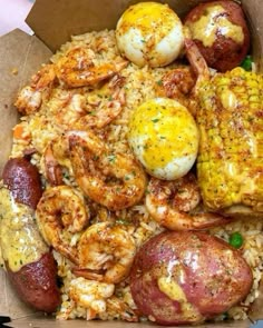 a box filled with rice, shrimp and corn on the cob next to potatoes