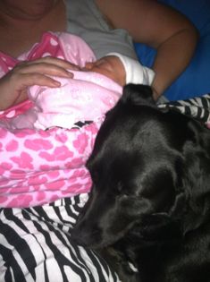 a black dog laying on top of a bed next to a woman holding a baby