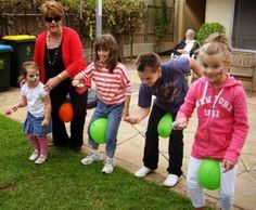 several children are playing with green balls in the yard while an adult watches from behind them