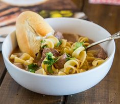 a white bowl filled with pasta and meat on top of a wooden table next to a book