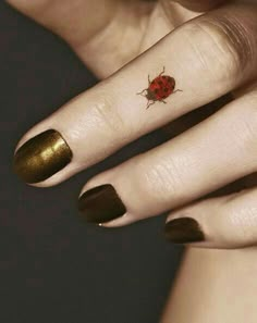 a ladybug tattoo on the finger of a woman's left hand with gold foil