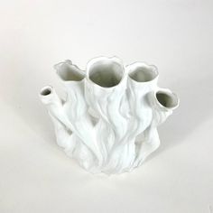 three white vases sitting side by side on a white surface, one is shaped like flames