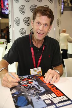 a man sitting at a table with a comic book in front of him and his name tag