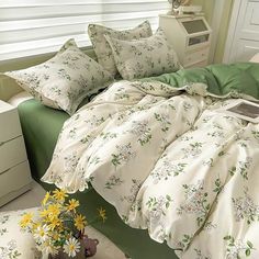 a bed with white and green sheets, pillows and flowers on the pillowcases