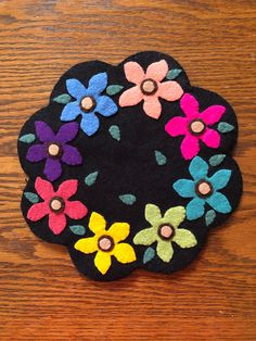 a black flower pot holder sitting on top of a wooden table covered in colorful felt flowers