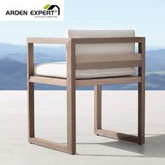 a wooden chair with white cushions on top of a cement floor next to a mountain