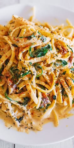 a white plate topped with pasta covered in sauce and spinach leafy garnish