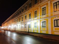 an empty street in front of a yellow building at night with lights shining on the windows