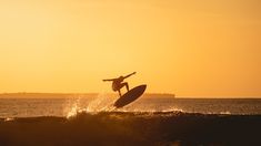 a person riding a surfboard on top of a wave in the ocean at sunset