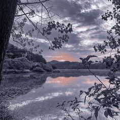 the sun is setting over a lake with trees in front of it and mountains in the distance