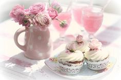 two cupcakes with frosting and pink flowers in a vase on a table