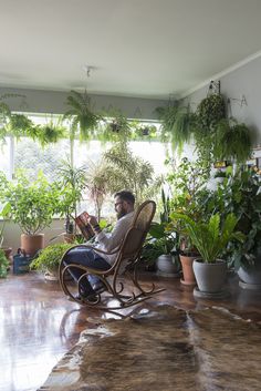 a man sitting in a rocking chair surrounded by potted plants