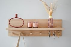 a wooden shelf with two glasses, a vase and several key hooks on it next to a handbag