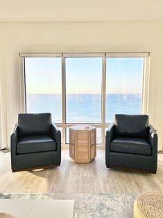 a living room with two chairs and a table in front of large windows overlooking the ocean