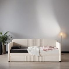 a white day bed sitting on top of a hard wood floor next to a potted plant