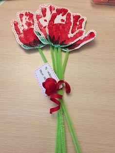 three red flowers with green stems and a tag on the end, tied to a wooden table