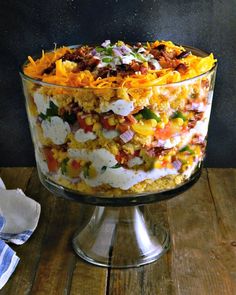 a large glass dish filled with food on top of a wooden table next to napkins