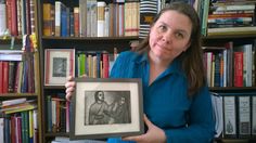 a woman holding up a framed drawing in front of a book shelf filled with books