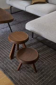 two wooden stools sitting on top of a rug in front of a gray couch