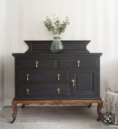 a black dresser with gold handles and drawers next to a vase filled with greenery