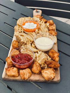 a wooden platter filled with fried food and dipping sauces on top of it