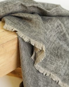 a wooden bench with a gray blanket on it's top and bottom part sitting next to a white wall