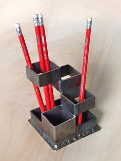 three red pencils are in a metal holder on a table with other pens and pencils