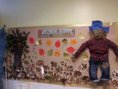 a scarecrow is standing on top of a bulletin board with autumn leaves and plants