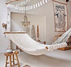 a hammock hanging from the ceiling in a room with white walls and wooden stools