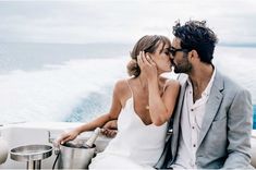 a man and woman kissing while sitting on a boat with the ocean in the background