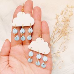 a person holding some kind of earrings in their hand with clouds and raindrops on them