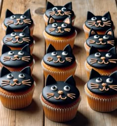 cupcakes with black icing and decorated cats on them sitting on a wooden table