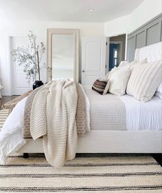 a white bed with pillows and blankets on top of it in a bedroom next to a mirror