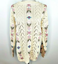 a white sweater with flowers on it hanging from a hanger next to a wall