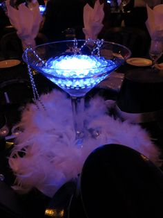 a martini glass with blue light in the middle and white feathers around it on a black table