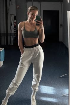 a woman taking a selfie with her cell phone in a gym room while wearing sweatpants