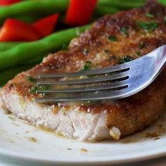 a piece of meat on a plate with a fork stuck into it and green beans in the background