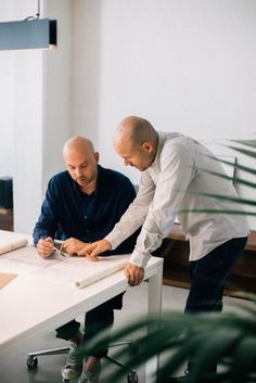 two men sitting at a white table working on some papers and writing something in front of them