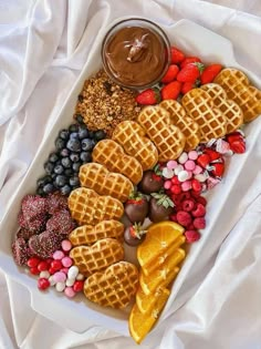 a white plate topped with waffles and fruit next to a bowl of chocolate