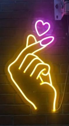 a neon sign with a hand holding a heart on it's side against a brick wall