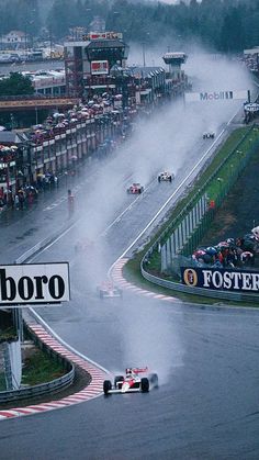 a group of cars driving down a race track with water pouring out of the air